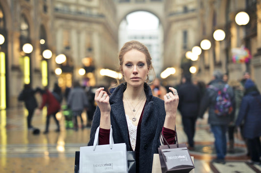 A woman standing in an elegant shopping arcade, holding multiple shopping bags, looking tired and overwhelmed while crowds blur behind her. Olly on Pexels
