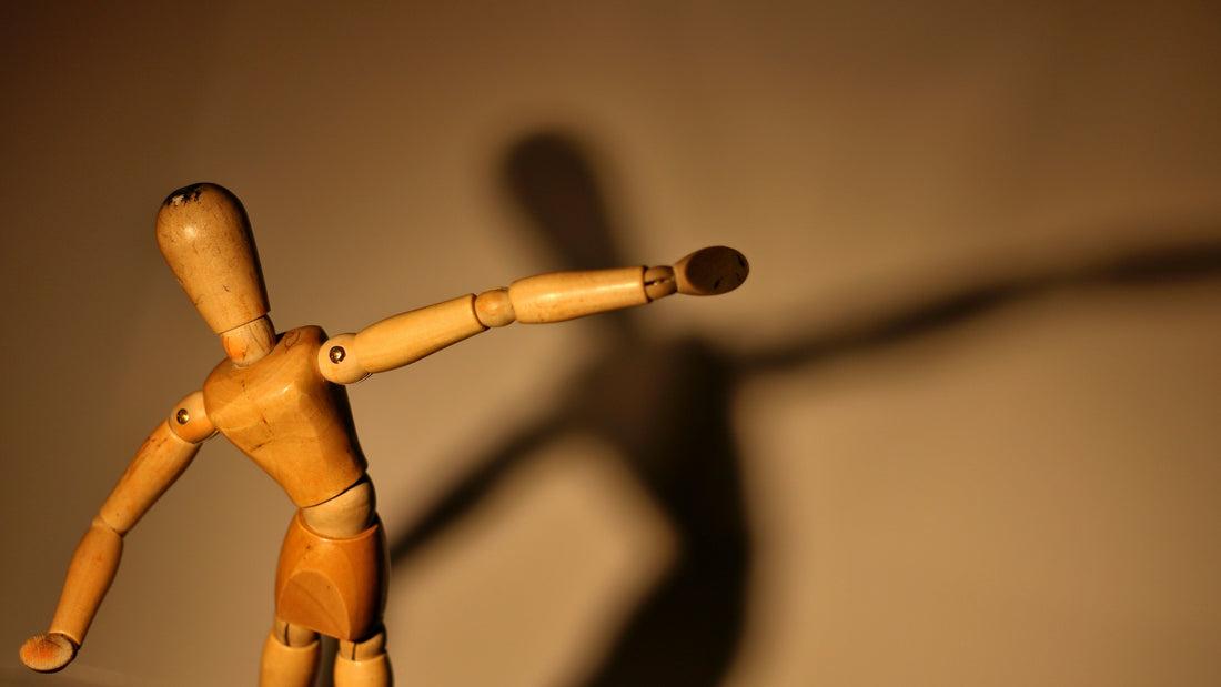 A wooden mannequin leaning into gentle movement, its shadow echoing behind it, suggesting the inner descent of awareness from the head into the body — like a pearl slowly sinking through golden oil into the deep center of the self.