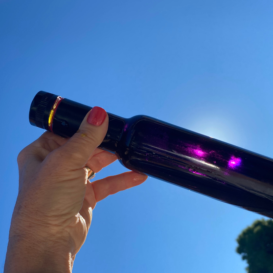 Hand holding dark violet glass bottle in sun.